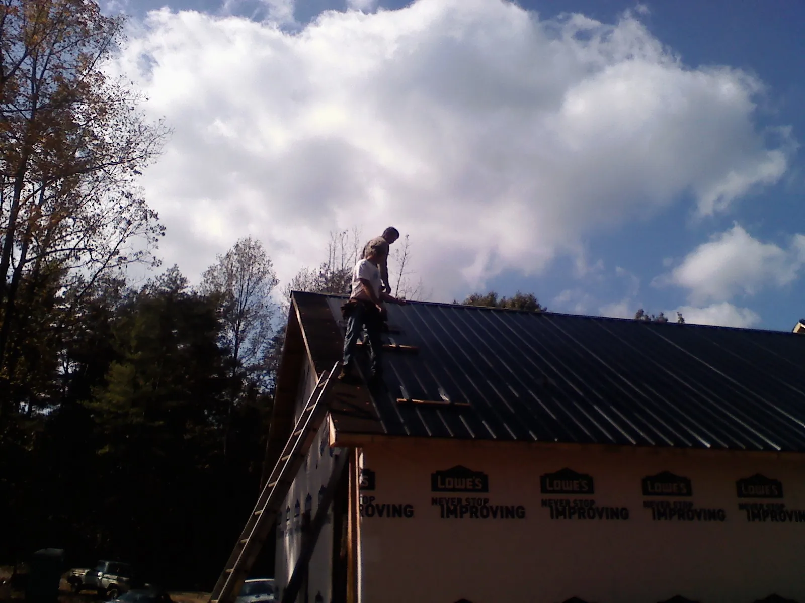 Roofer fastening dark metal panels high against a cloudy sky, from a Roof Inspection job in Nashua