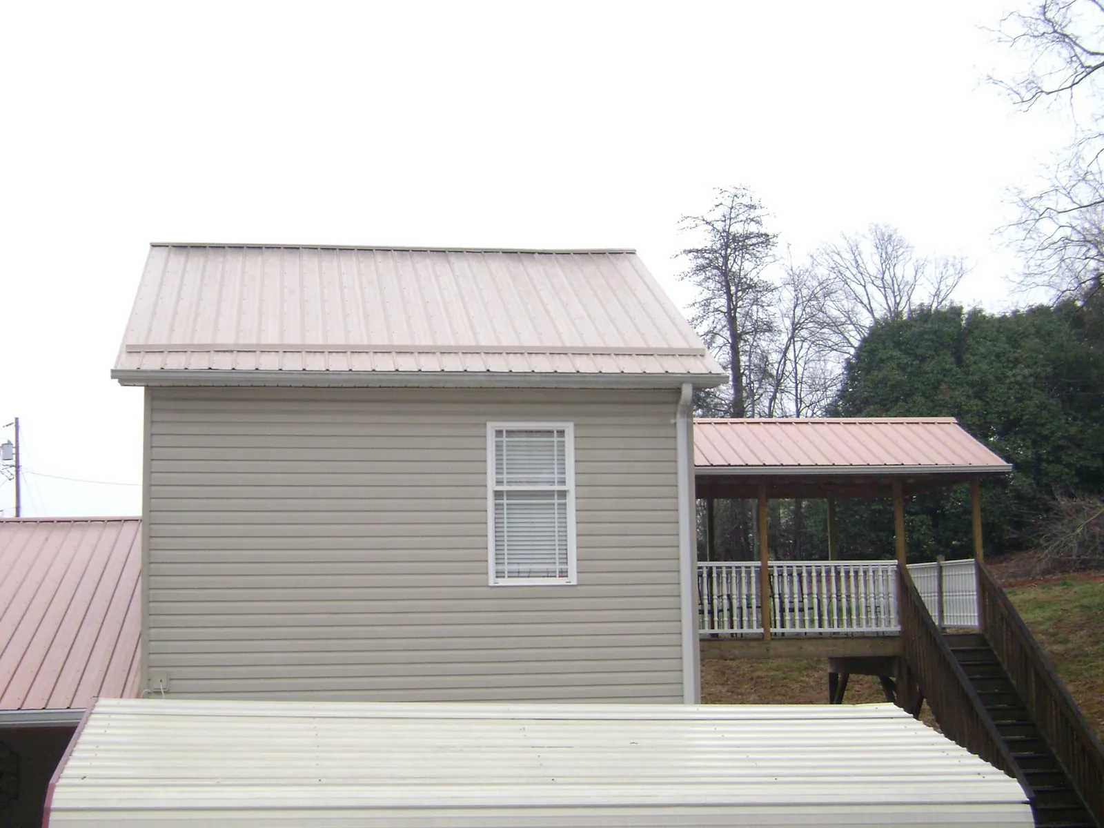 Tan metal roofs on a two story addition and attached porch, from a Roof Replacement job in Nashua